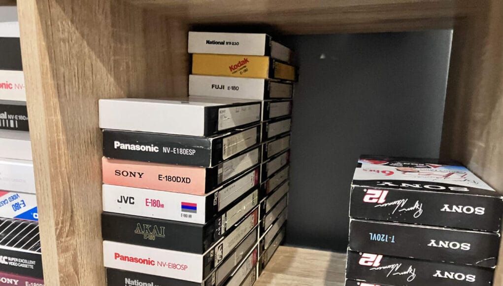 how-long-do-vhs-tapes-last-tapes-on-shelf A shelf of VHS tapes kept in a home office, the kind of everyday storage that decides how long do VHS tapes last.